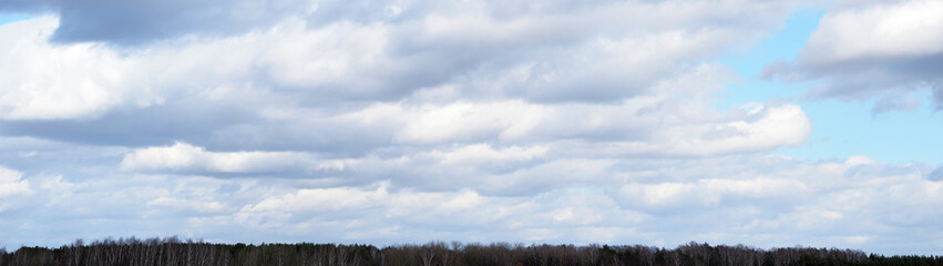 Fototapeta na wymiar horizontal panorama. blue sky with white clouds and treetops