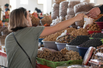 European she-tourist buys sweets and nuts on the Food market (bazaar). Bukhara, Uzbekistan, Central Asia. - obrazy, fototapety, plakaty