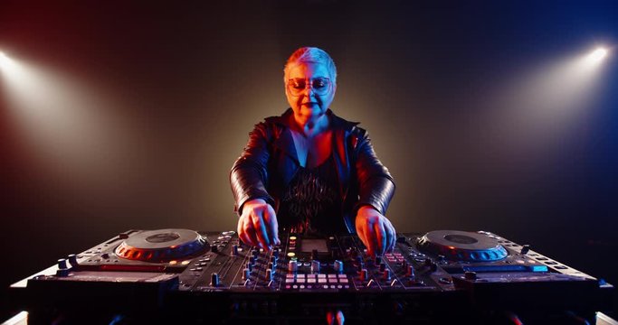 Funny grandma is a dj. Authentic mature woman in cool outfit working at turntables in a nightclub, rocking the party up 4k footage