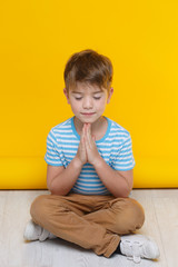 Fototapeta na wymiar Little cute boy meditates sitting on a yellow background.