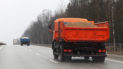 Orange loaded dump truck with gravel drive on highway road at spring day