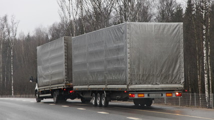 Compact awning truck with gray tented three-axle trailer drive on country asphali highway road on autumn day