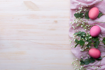 Pink chicken eggs in sprigs of eucalyptus and gypsophila flowers on a white wooden background....