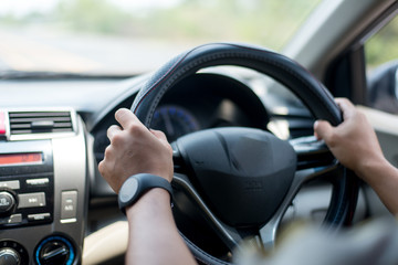 A young Asian man drives a car on a daytime road.