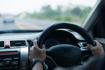 A young Asian man drives a car on a daytime road.