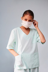 A young nurse or assistant in medical clothing puts on a mask.