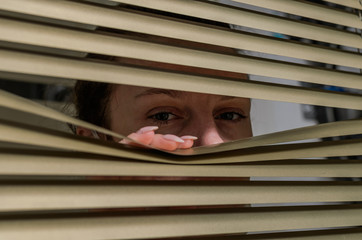 Young woman looking out the window through the blinds