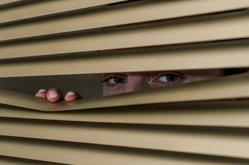 Young woman looking out the window through the blinds