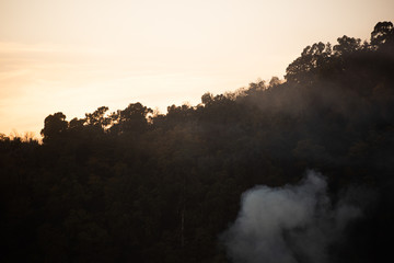 Smoke on background with mountains covered with trees with the setting sun