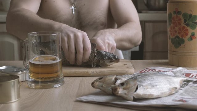 Brutal man drinking beer and cutting dried fish. Glass of cold fresh lager beer. Sun dried salted fish snack to beer. Taranka.