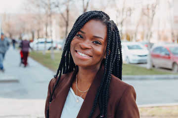 Close up portrait of a beautiful young african american woman with pigtails hairstyle in a brown business suit walks along spring streets