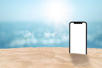 Business Communication and Summer Travel Trip Concept : Black smartphone with blank white screen on sand beach with blurry seascape view and bokeh sunlight in background.