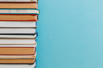 A simple composition of many hardback books, raw books on a wooden table and a bright blue background. Going back to school. Copy space. Education.