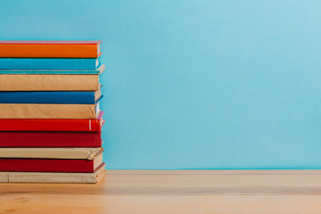 A simple composition of many hardback books, raw books on a wooden table and a bright blue background. Going back to school. Copy space. Education.