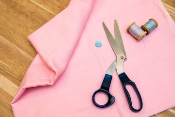 Set of tailoring accessories. Close up of a stack of folded pink fabric, sewing scissors, and spools of thread
