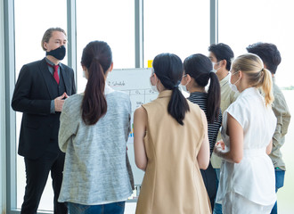 Obraz premium Small business startup multiracial brainstorm meeting with chart paper board everyone mask for covid-19 protection coronavirus flu prevent healthy ideas concept office background.