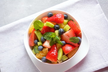 Bowl of healthy fresh colorful fruit salad on wooden background. Top view.Fruit salad with strawberry, blueberry, sweet cherry, kiwi.Vegetarian food concept. Rustic wooden background