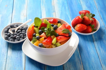 Bowl of healthy fresh colorful fruit salad on wooden background. Top view.Fruit salad with strawberry, blueberry, sweet cherry, kiwi.Vegetarian food concept. Rustic wooden background