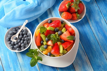Bowl of healthy fresh colorful fruit salad on wooden background. Top view.Fruit salad with strawberry, blueberry, sweet cherry, kiwi.Vegetarian food concept. Rustic wooden background
