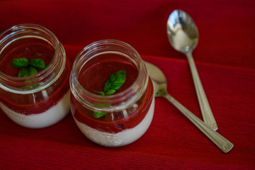Tasty fragrant panacotta with strawberry compote decorated with fresh basil in glass jars next to...