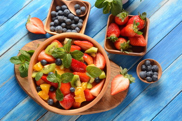 Bowl of healthy fresh colorful fruit salad on wooden background. Top view.Fruit salad with strawberry, blueberry, sweet cherry, kiwi.Vegetarian food concept. Rustic wooden background