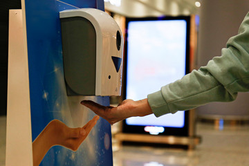 Macro shot of young woman using automatic hand sanitizer dispenser at the international airport...