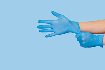The doctor puts on sterile gloves on a blue background. Infection control concept. Danger of spread...