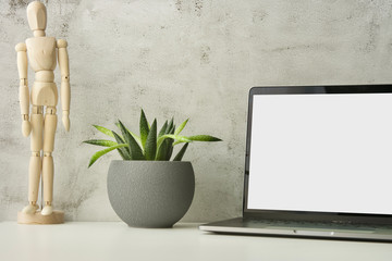 Work table with laptop with white clean screen, flower and wooden drawing figure