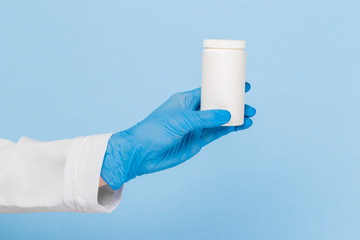 Doctor's hands in sterile gloves hold a jar of pills on a blue background. Infection control concept.