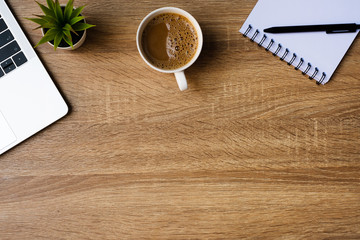 desk office with laptop, blank notepad, coffee cup and pen on wood table. Flat lay top view copy spce.