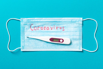 Top view of protective medical mask and a thermometer on blue background. Coronavirus word. Ncov...
