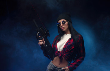 Fototapeta premium a girl in a checked shirt on a dark background with an automatic rifle