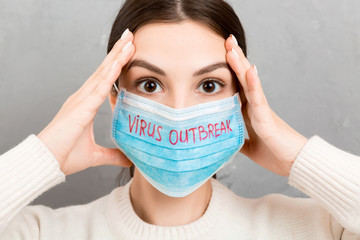 Portrait of pretty shocked woman wearing medical mask with virus outbreak text at gray cement background. Coronavirus concept. Respiratory protection