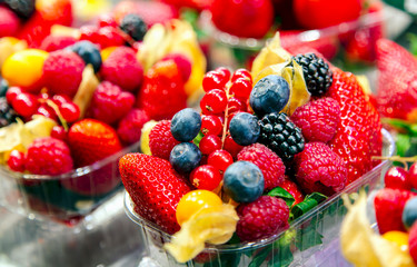 Varied assortment of fresh berries for dessert - raspberries, strawberries, blueberries, blackberry in a basket at a farmers market.