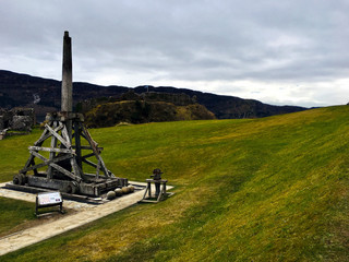 Fototapeta na wymiar Old Catapult staying on the grass with hills in the background on a cloudy day in Scotland - Architecture Photography