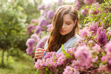 Young pretty girl in closed eyes enjoys the smell of lilac in the early morning in the garden..