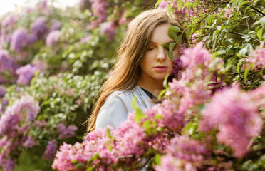 Young pretty girl in closed eyes enjoys the smell of lilac in the early morning in the garden..