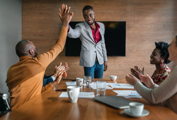 Two African businessmen giving high five while diverse South African coworkers clapping in congratulations