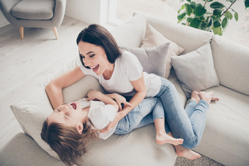 Top above high angle view photo of ideal candid mother daughter relationship mommy and her kid play tickle lay divan in apartment indoors - obrazy, fototapety, plakaty