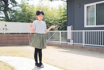 庭で縄跳びの練習をする小学生の女の子 - obrazy, fototapety, plakaty