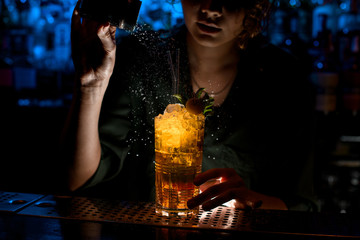 Woman bartender at dark bar decorate by powder glass with cocktail.