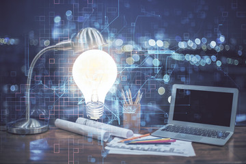 Computer on desktop in office with bulb icon hologram. Multi exposure. Concept of idea.