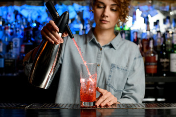 young bartender woman actively pouring cocktail using steel siphon