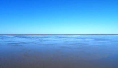 Coastal horizon with a clear blue sky reflected on shimmering beach with selective focus.