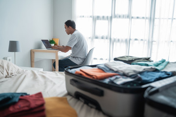 asian young man checking departure schedules via online application after preparing and put her clothes in the suitcase