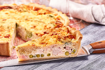 quiche with ham vegetables chicken on a colorful wooden background, napkin, textile, knife
