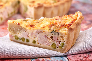 quiche with ham vegetables chicken on a colorful wooden background, napkin, textile, knife