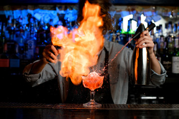 Woman bartender spraying on fire around cocktail glass on bar counter