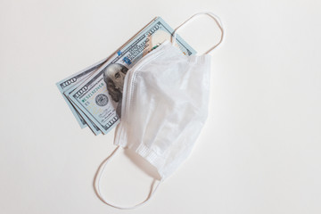 Healthcare cost concept. US Dollars with surgical mask with rubber ear straps on white background. The inscription medical protective mask with dollars. Image of a blue face mask and money.