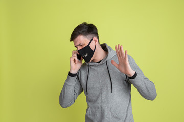 Talking on phone. Caucasian man's portrait isolated on yellow studio background. Freaky male model in black face mask. Concept of human emotions, facial expression, sales, ad. Unusual appearance.